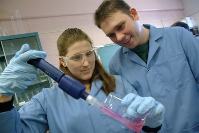 Two young students in lab coats running an experiment