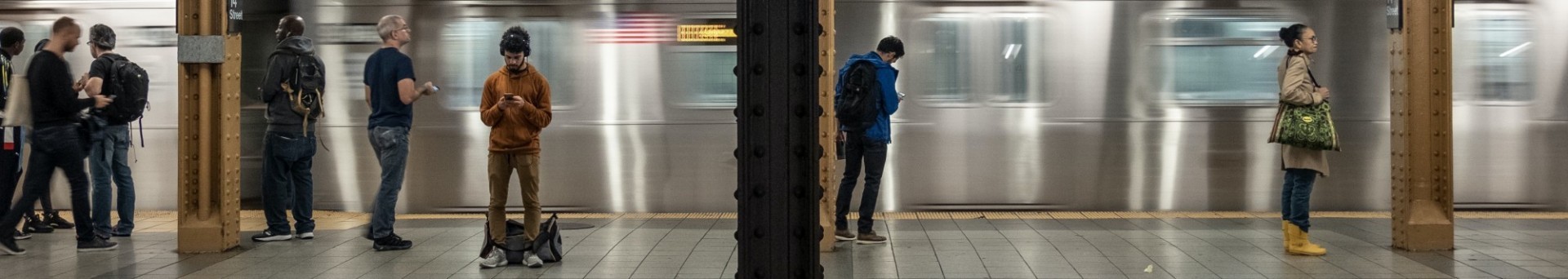 Image of NYC subway platform with blurred train coming into the station; several commuters are waiting on the platform