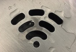 Image of the wifi symbol: a dot with lines radiating above it in a cirular pattern. This image shows a black symbol on a grey, metallic background with clear water droplets scattered atop